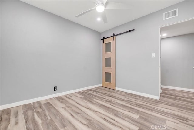 empty room featuring light hardwood / wood-style flooring, a barn door, and ceiling fan