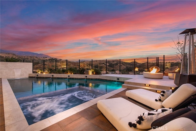 pool at dusk with a jacuzzi, a mountain view, and a fire pit