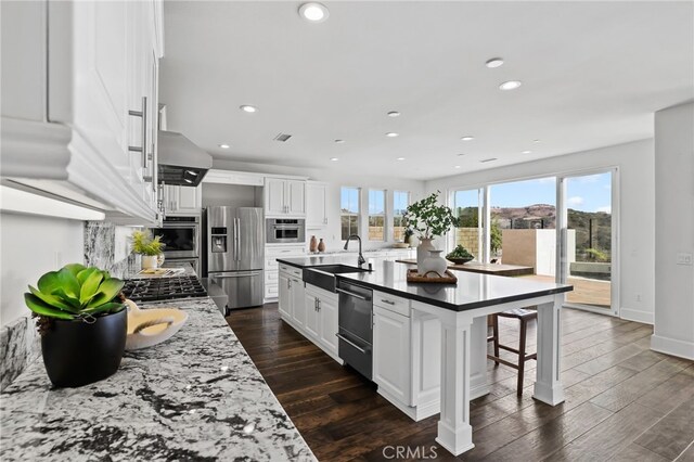 kitchen with appliances with stainless steel finishes, sink, white cabinets, a kitchen breakfast bar, and a center island with sink