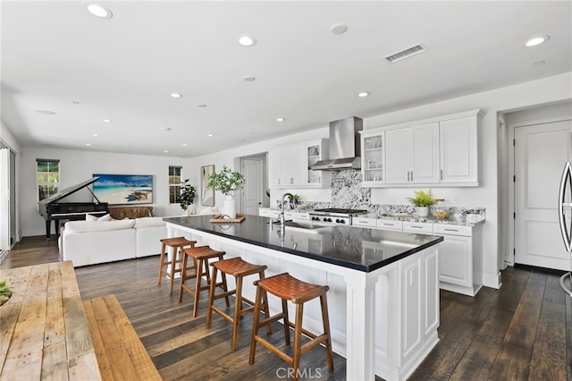 kitchen featuring wall chimney range hood, sink, a breakfast bar, white cabinetry, and a kitchen island with sink