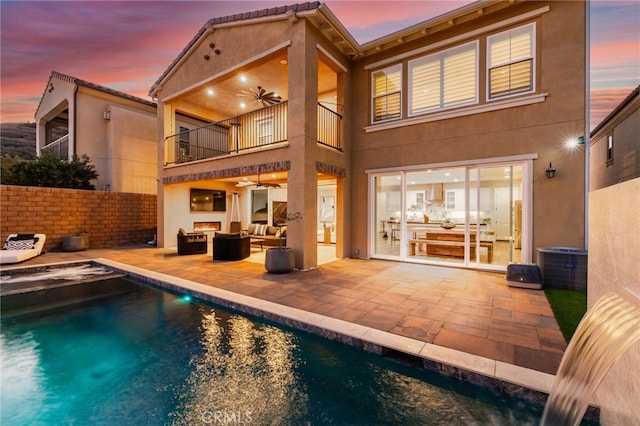 back house at dusk with ceiling fan, a balcony, an outdoor hangout area, and a patio area