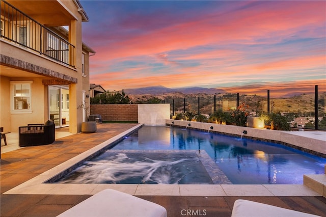 pool at dusk featuring a mountain view and pool water feature