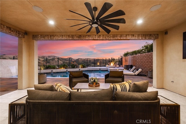 patio terrace at dusk with ceiling fan, an outdoor hangout area, a fenced in pool, and a mountain view