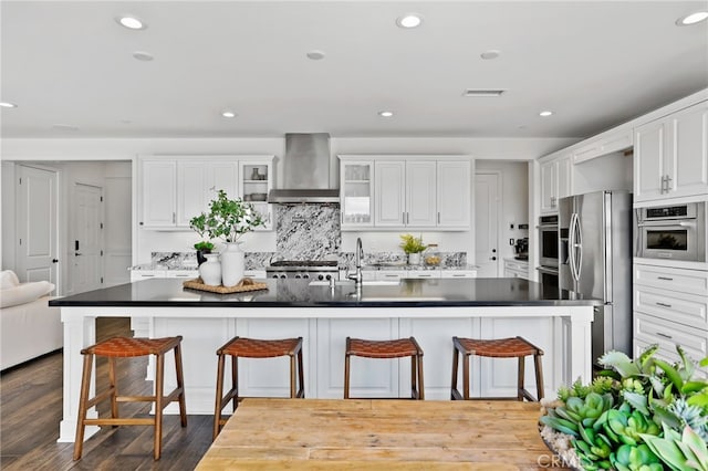 kitchen featuring white cabinetry, stainless steel refrigerator with ice dispenser, a kitchen bar, and wall chimney exhaust hood