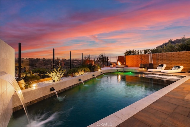 pool at dusk featuring a patio and pool water feature