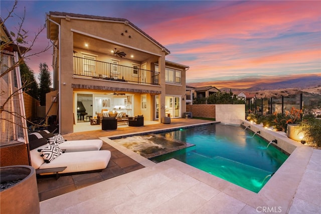 back house at dusk with a fenced in pool, outdoor lounge area, a patio, pool water feature, and a balcony