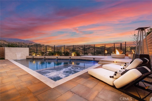 pool at dusk with a mountain view, a fire pit, and a patio