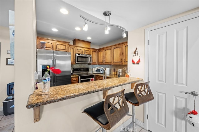 kitchen with light stone counters, stainless steel appliances, a breakfast bar, and kitchen peninsula