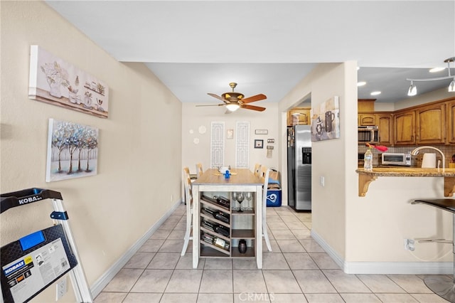 kitchen featuring a breakfast bar area, light tile patterned floors, ceiling fan, stainless steel appliances, and light stone countertops