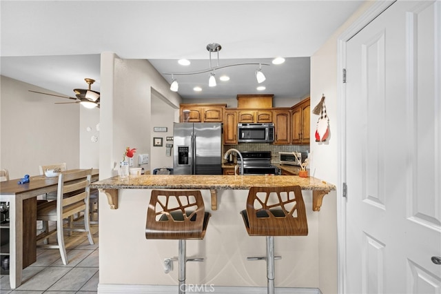 kitchen with light tile patterned floors, a kitchen breakfast bar, kitchen peninsula, stainless steel appliances, and decorative backsplash