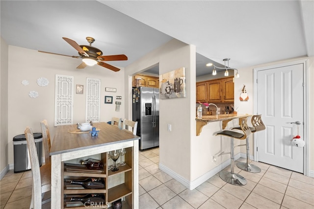 kitchen with light stone counters, kitchen peninsula, stainless steel fridge with ice dispenser, and light tile patterned floors