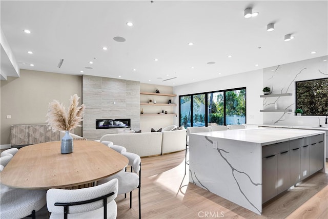 kitchen with gray cabinets, a tiled fireplace, a large island, light hardwood / wood-style floors, and light stone countertops