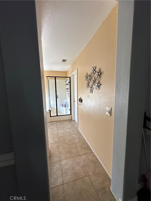 hall with a textured ceiling and light tile patterned floors