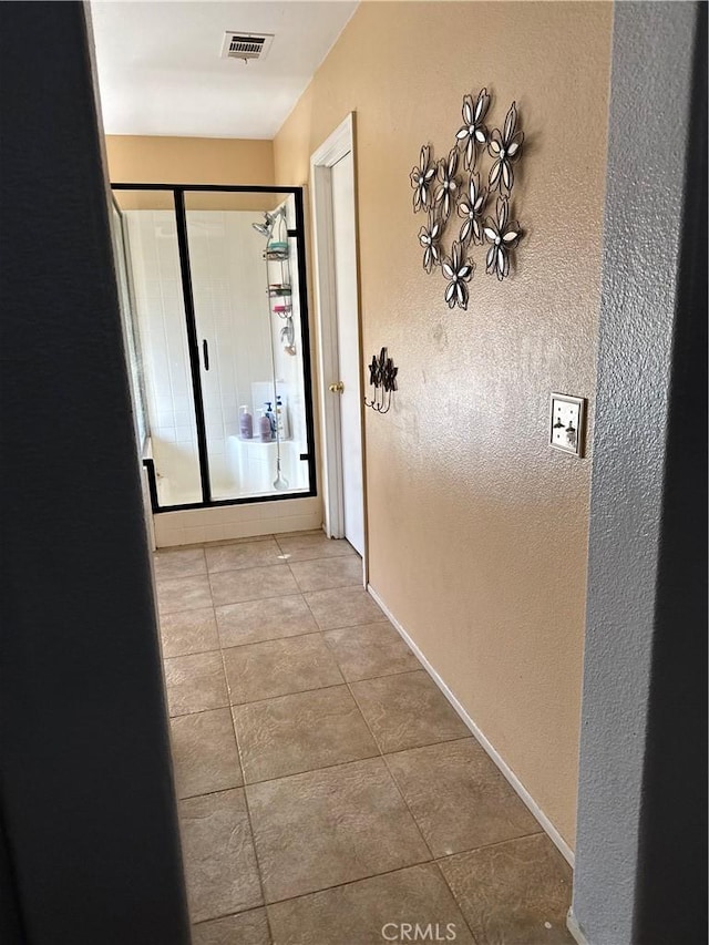 hall with tile patterned floors, a textured wall, baseboards, and visible vents