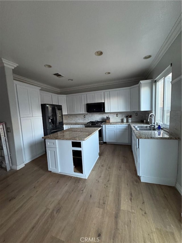 kitchen with a sink, a center island, white cabinetry, ornamental molding, and black appliances
