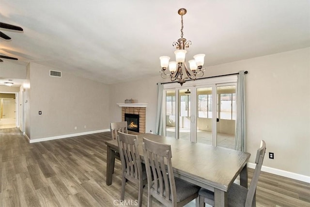 dining space featuring a fireplace, dark hardwood / wood-style floors, and ceiling fan with notable chandelier