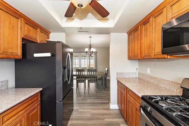 kitchen featuring appliances with stainless steel finishes, ceiling fan with notable chandelier, pendant lighting, light hardwood / wood-style floors, and a tray ceiling