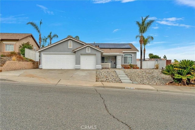 ranch-style home with a garage, roof mounted solar panels, stucco siding, and fence