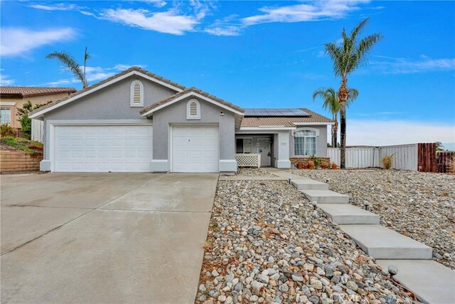 single story home featuring fence, solar panels, an attached garage, concrete driveway, and stucco siding