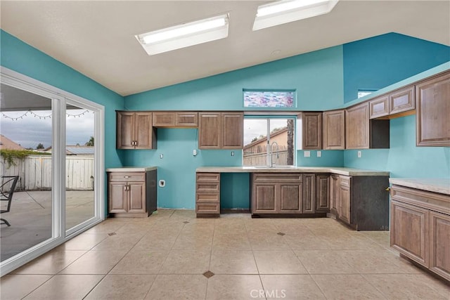 kitchen featuring brown cabinets, light countertops, a sink, light tile patterned flooring, and high vaulted ceiling