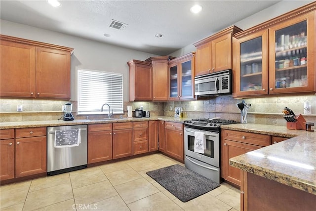 kitchen featuring visible vents, brown cabinets, light stone countertops, stainless steel appliances, and a sink