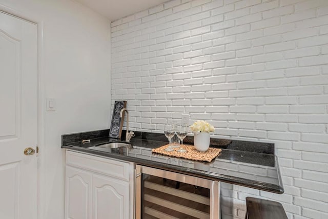 bar featuring white cabinetry, sink, beverage cooler, and brick wall