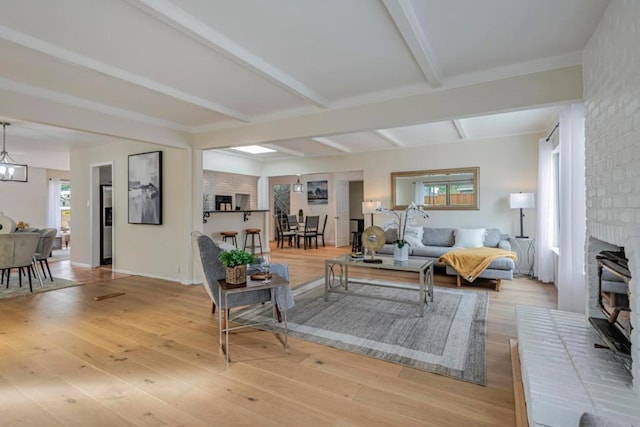 living room with an inviting chandelier, a fireplace, beam ceiling, and light wood-type flooring