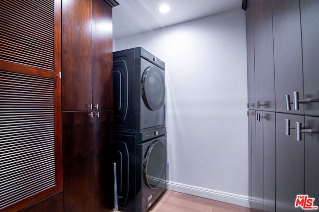 washroom with cabinets, stacked washer and clothes dryer, and light hardwood / wood-style floors