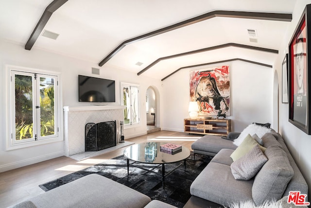 living room featuring a tile fireplace, vaulted ceiling with beams, and light hardwood / wood-style floors