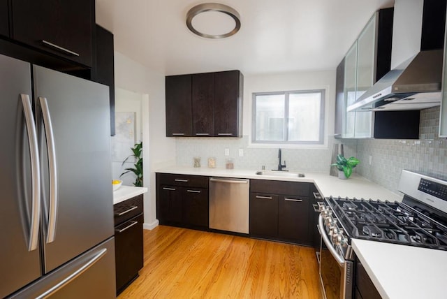 kitchen featuring sink, dark brown cabinets, light wood-type flooring, stainless steel appliances, and wall chimney range hood