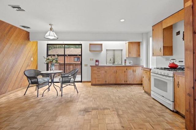 kitchen featuring white gas range, decorative light fixtures, light parquet floors, and wood walls