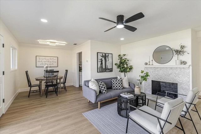 living room featuring a tile fireplace, ceiling fan, and light wood-type flooring