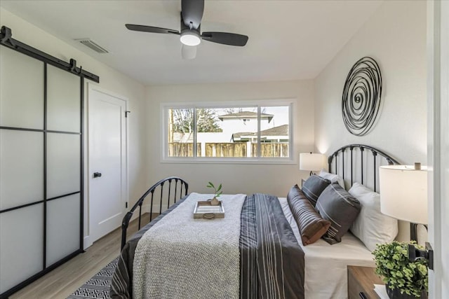 bedroom featuring ceiling fan, a barn door, and light hardwood / wood-style floors