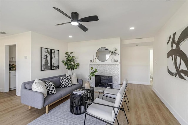 living room featuring a tile fireplace, ceiling fan, and light wood-type flooring