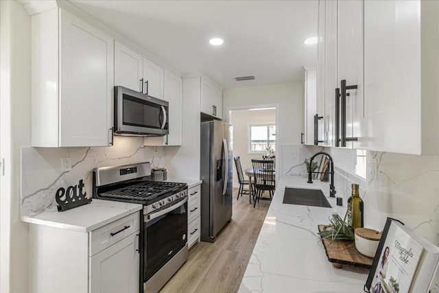 kitchen with light stone counters, appliances with stainless steel finishes, sink, and white cabinets