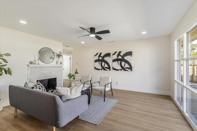 living room featuring light hardwood / wood-style flooring, a tile fireplace, and ceiling fan