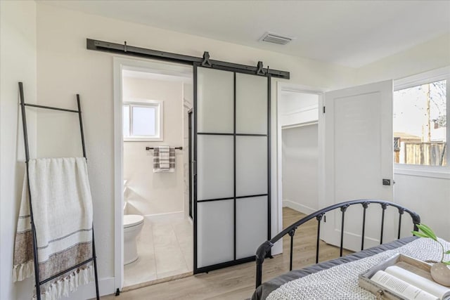 bedroom with light hardwood / wood-style floors, a barn door, and ensuite bathroom