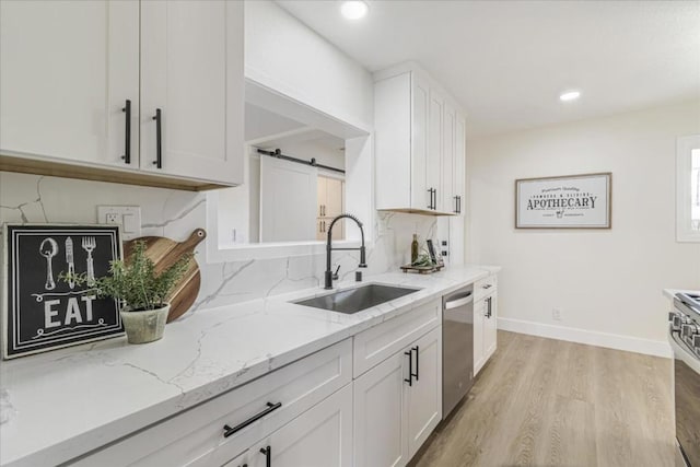 kitchen with sink, light stone counters, stainless steel dishwasher, a barn door, and white cabinets