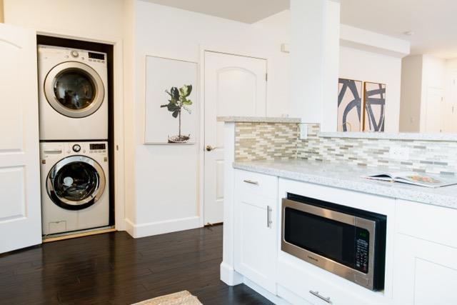 kitchen with light stone countertops, stacked washer and clothes dryer, stainless steel microwave, and white cabinets