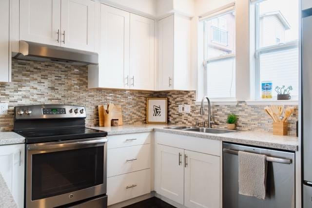 kitchen featuring sink, white cabinetry, light stone counters, appliances with stainless steel finishes, and decorative backsplash