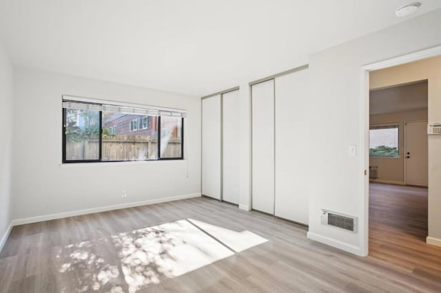 unfurnished bedroom with multiple windows, two closets, and light hardwood / wood-style flooring