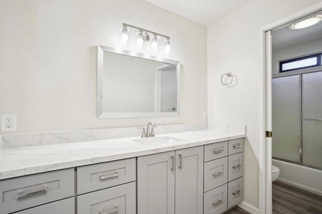 full bathroom featuring hardwood / wood-style flooring, vanity, toilet, and combined bath / shower with glass door