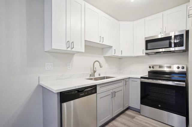 kitchen featuring sink, light hardwood / wood-style flooring, stainless steel appliances, light stone countertops, and white cabinets