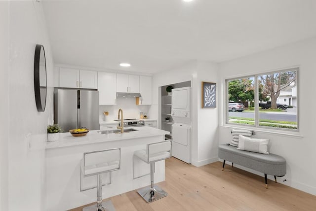 kitchen with light hardwood / wood-style flooring, a breakfast bar, white cabinetry, stainless steel appliances, and stacked washer and clothes dryer