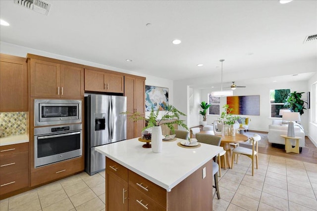 kitchen with appliances with stainless steel finishes, a center island, light tile patterned floors, and decorative light fixtures