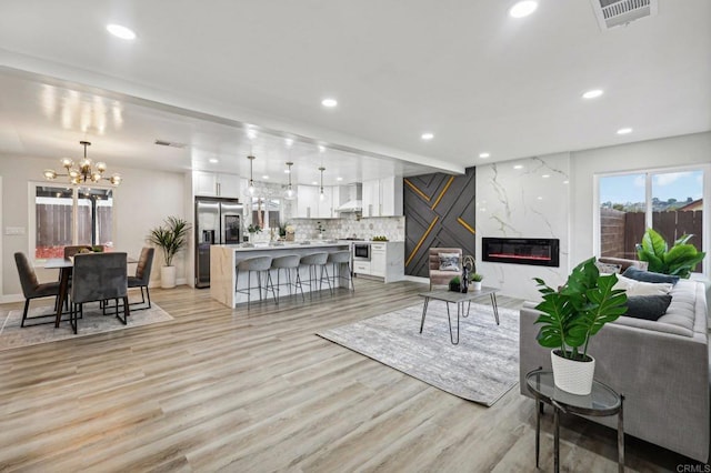 living room with an inviting chandelier, a high end fireplace, and light hardwood / wood-style floors