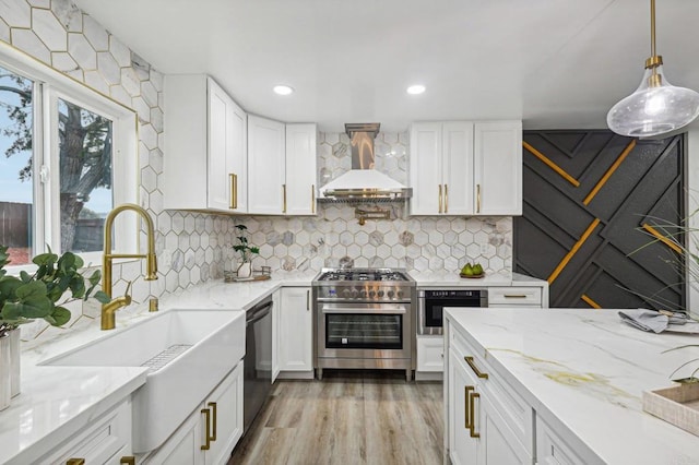 kitchen with light stone counters, stainless steel appliances, white cabinets, wall chimney exhaust hood, and decorative light fixtures