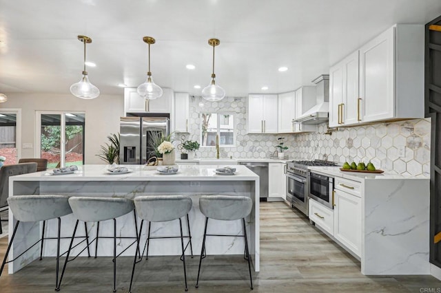 kitchen featuring white cabinets, wall chimney exhaust hood, a kitchen island, hanging light fixtures, and stainless steel appliances