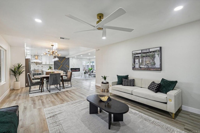 living room featuring recessed lighting, ceiling fan with notable chandelier, visible vents, baseboards, and light wood-type flooring