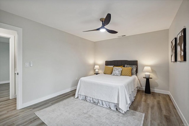 bedroom featuring a ceiling fan, baseboards, visible vents, and wood finished floors